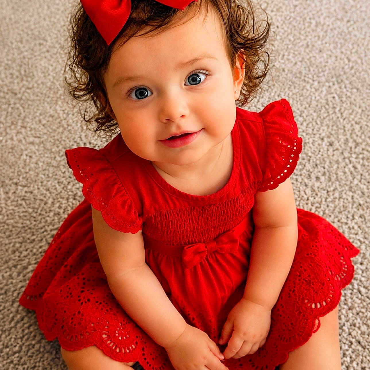 Hazel is registered to the contest to win money with this photo: toddler, child, baby, red_dress, bow, curly_hair, carpet, smiling, cute, portrait, sitting, indoors, fashion, happy, young_child, person, eyes, face, hands, cute_outfit