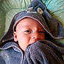 baby, towel, hooded_towel, face, eyes, blanket, bedspread, infant, soft_texture, curious, child, wrapped, cozy, indoor, closeup, young_child, cute, comfort, nibble, resting