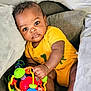 baby, infant, child, yellow_onesie, toy, colorful_toy, cushion, sofa, indoor, curious, hand, foot, face, eyes, skin, play, relax, comfort, young, portrait