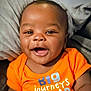 baby, child, smiling, orange_shirt, face, happy, infant, person, portrait, cushion, cozy, closeup, sitting, cute, skin, head, eyebrows, eyes, mouth, indoor