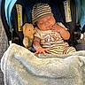 Luis joined the competition — help win amazing prizes! baby, sleeping, car_seat, plush_toy, blanket, striped_clothing, hat, footwear, floor, person, infant, cozy, child, cute, indoors, soft_texture, resting, napping, toddler, peaceful