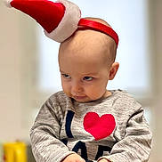Callen a rejoint le concours — aidez-le/la à gagner de superbes lots ! toddler, child, baby, headband, santa_hat, sweater, heart_symbol, indoor, cute, expression, face, hands, holding, portrait, clothing, playful, smirk, young_child, person, holiday