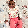 baby, infant, child, smiling, portrait, lying_down, floral_clothing, headband, bow, bib, pink_pants, blanket, butterfly_pattern, indoors, close_up, face, hands, happy, colorful, candid