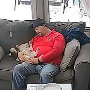 Krypto joined the competition — help win amazing prizes! beanie, casual_clothing, couch, cozy, dog, gray_couch, home, indoor, living_room, man, napping, pet, pillows, red_shirt, relaxing, resting, seated, sleeping, window, winter