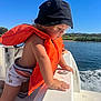adventure, blue_sky, boat, child, clothing, curious, daylight, hat, life_jacket, nature, outdoor, person, river, side_view, sitting, summer, sunny, toddler, water, watercraft