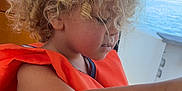 Heaven a rejoint le concours — aidez-le/la à gagner de superbes lots ! boat, casual_clothing, child, curly_hair, daylight, focused, indoor, life_jacket, nature, nautical, orange, portrait, safety, sea, side_profile, summer, vacation, water, window, young_child