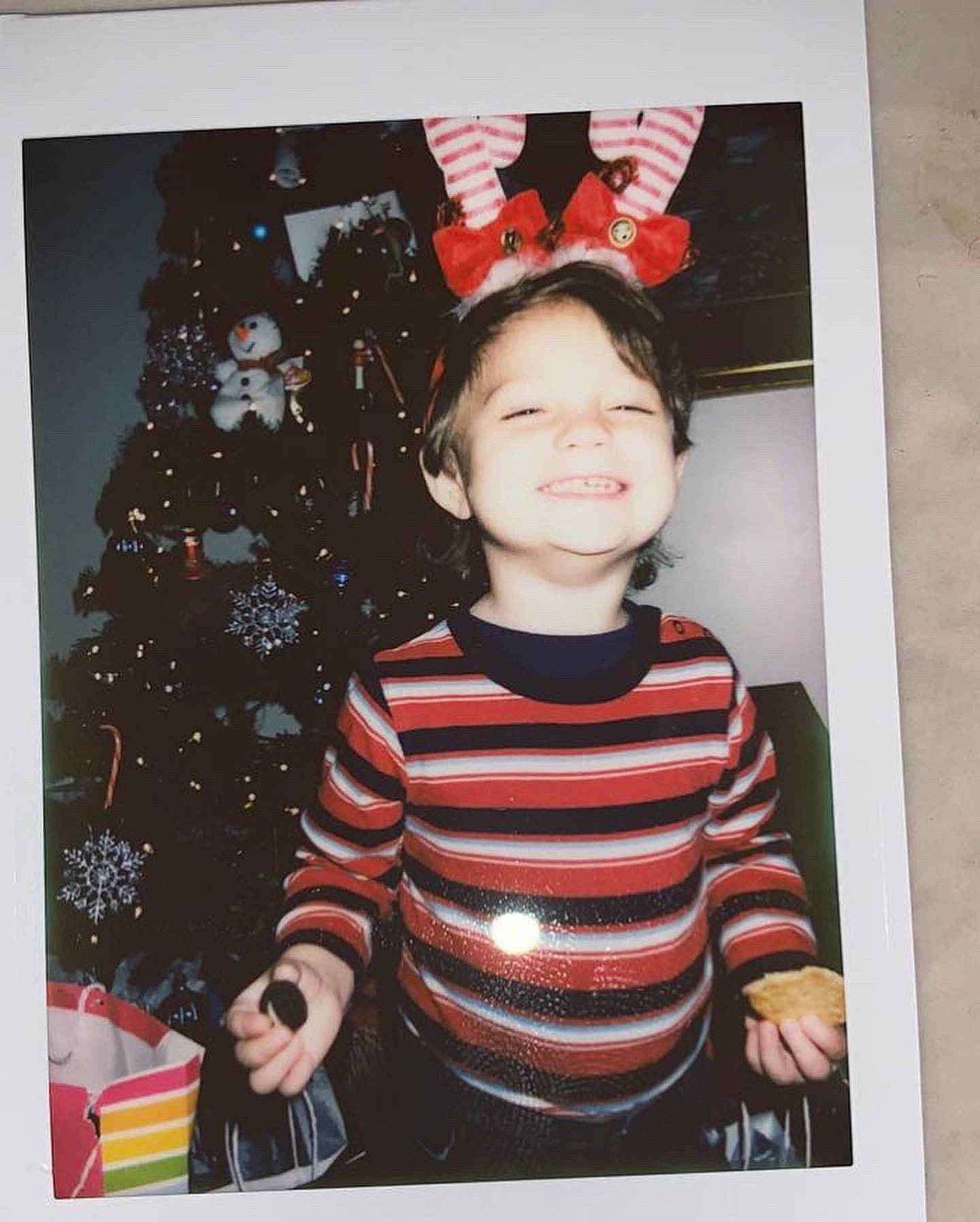Ryker is registered to the contest to win money with this photo: baby_toddler_clothing, carmine, christmas, christmas_decoration, christmas_ornament, christmas_tree, event, happy, holiday, holiday_ornament, joy, ornament, pattern, person, rectangle, red, room, sleeve, smile, t_shirt