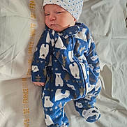 Louis participe au concours pour gagner de l'argent avec cette photo : baby, bear_pattern, bed, blue_clothing, child, cute, footwear, hat, indoors, infant, lying_down, newborn, onesie, sheet, sleepwear, slippers, soft_texture, stars, text_on_sheet, white_hat
