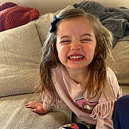 Laiklyn is registered to the contest to win money with this photo: child, girl, smiling, happy, couch, indoor, clothing, long_hair, blue_bow, fringe, pants, beige, blanket, casual, portrait, person, expression, home, cute, joyful