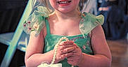 Laiklyn is registered to the contest to win money with this photo: child, girl, smiling, green_dress, flowers, hair_accessory, pearl_purse, party, indoor, people, background, string_lights, happy, portrait, holding, cute, fashion, celebration, event, young