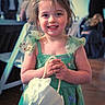 child, girl, smiling, green_dress, flowers, hair_accessory, pearl_purse, party, indoor, people, background, string_lights, happy, portrait, holding, cute, fashion, celebration, event, young