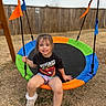 child, swing, playground, outdoor, smiling, happy, fence, grass, casual_clothing, shorts, sneakers, toy, playtime, summer, young, girl, colorful, rope, yard, fun