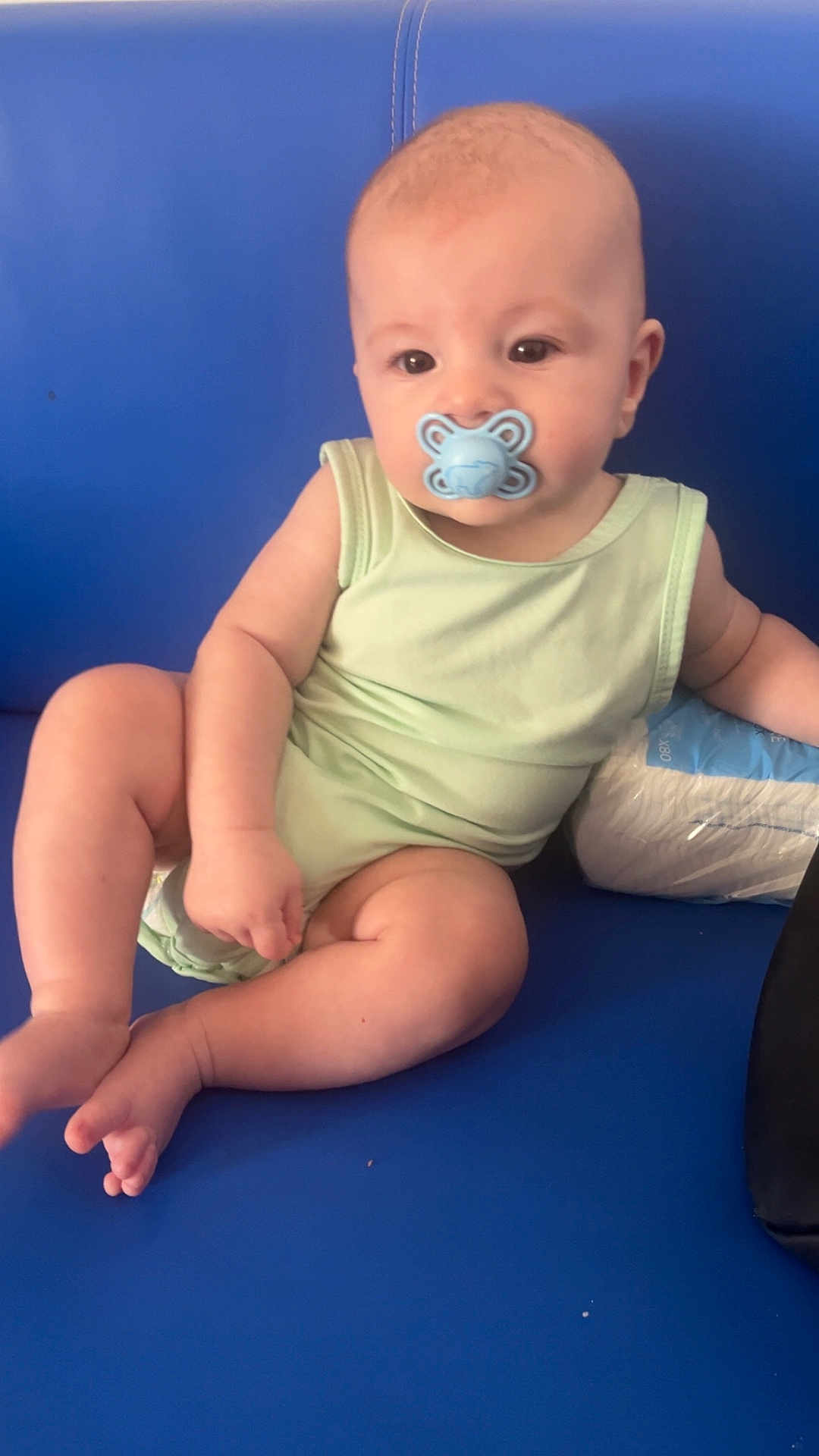 Alessio participe au concours pour gagner de l'argent avec cette photo : baby, infant, pacifier, blue_couch, green_clothing, diapers, sitting, cute, child, indoor, plump, skin, person, furniture, relaxed, chubby_arms, legs, head, expression, comfort