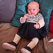 Ophélie participe au concours pour gagner de l'argent avec cette photo : baby, infant, child, couch, pillow, clothing, dress, tights, shoes, striped, sitting, smiling, cute, indoor, soft, comfortable, person, portrait, young, home