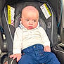 baby, child, car_seat, infant, white_shirt, blue_pants, seated, indoor, person, face, hand, clothing, safety, warning_label, head, skin, expression, light, portrait, young
