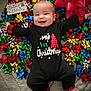 baby, infant, smiling, christmas, holiday, festive, onesie, black_clothing, red_plaid, gift_bows, large_bow, bed, blanket, special_delivery_sign, happy, celebration, seasonal, cute, child, portrait