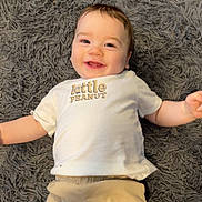 Grayson joined the competition — help win amazing prizes! baby, infant, smile, happy, child, lying_down, white_shirt, beige_shorts, carpet, gray_rug, cute, portrait, indoor, person, young_child, baby_clothes, toddler, happy_face, small_child, relaxed