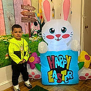 Kaison is registered to the contest to win money with this photo: child, boy, indoor, inflatable, easter_bunny, holiday, decoration, colorful, happy_easter, sign, flowers, wall_art, yellow_jacket, sneakers, floor, wooden_floor, smiling, standing, playful, celebration