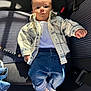 baby, bead_chain, black_stripes, car_seat, casual_clothing, child, fabric, indoor, jeans, keys, name_beads, person, plaid_jacket, portrait, rolled_jeans, seatbelt, shadow, sock, sunlight, white_shirt