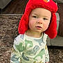 toddler, child, hat, red_hat, elmo, indoor, carpet, dinosaur_shirt, long_sleeve, curious, standing, face, expression, young_child, casual_clothing, floor, furniture, sofa, person, portrait