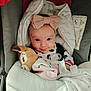 baby, infant, bow, headband, blanket, car_seat, plush_toy, pacifier, smile, clothing, cute, face, child, indoors, comfort, warm, soft_toy, seatbelt, nap_time, adorable