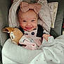 baby, smiling, bow, headband, car_seat, blanket, plush_toy, happy, infant, cute, child, clothing, fabric, indoors, portrait, person, cozy, soft, snuggled, joy