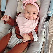Ambre a rejoint le concours — aidez-le/la à gagner de superbes lots ! baby, infant, smiling, headband, pink, bib, brown_clothing, baby_carrier, cute, happy, child, face, hand, fabric, seat, comfort, indoors, portrait, person, soft
