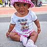baby, child, infant, portrait, sitting, outdoor, sidewalk, street, urban, hat, pink_hat, socks, pink_clothing, t_shirt, graphic_shirt, smiling, curious, fashion, storefront, daylight