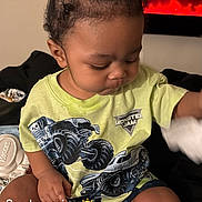Taytum joined the competition — help win amazing prizes! toddler, child, indoor, sitting, tshirt, monster_jam, hair_bun, toy, fireplace, plant, shelf, white_socks, black_bedspread, hand, face, cute, focused, morning, text_overlay, cozy