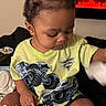 toddler, child, indoor, sitting, tshirt, monster_jam, hair_bun, toy, fireplace, plant, shelf, white_socks, black_bedspread, hand, face, cute, focused, morning, text_overlay, cozy