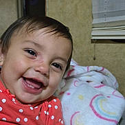 Kapri is registered to the contest to win money with this photo: toddler, child, smiling, face, blanket, polka_dot, red_clothing, indoor, window_blind, happy, cute, baby, portrait, head, skin, person, sitting, fabric, cozy, colorful