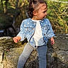 toddler, child, denim_jacket, sneakers, leggings, stone_wall, outdoor, nature, greenery, sunlight, trees, curious, portrait, casual_clothing, young_child, side_view, daylight, person, cute, sitting
