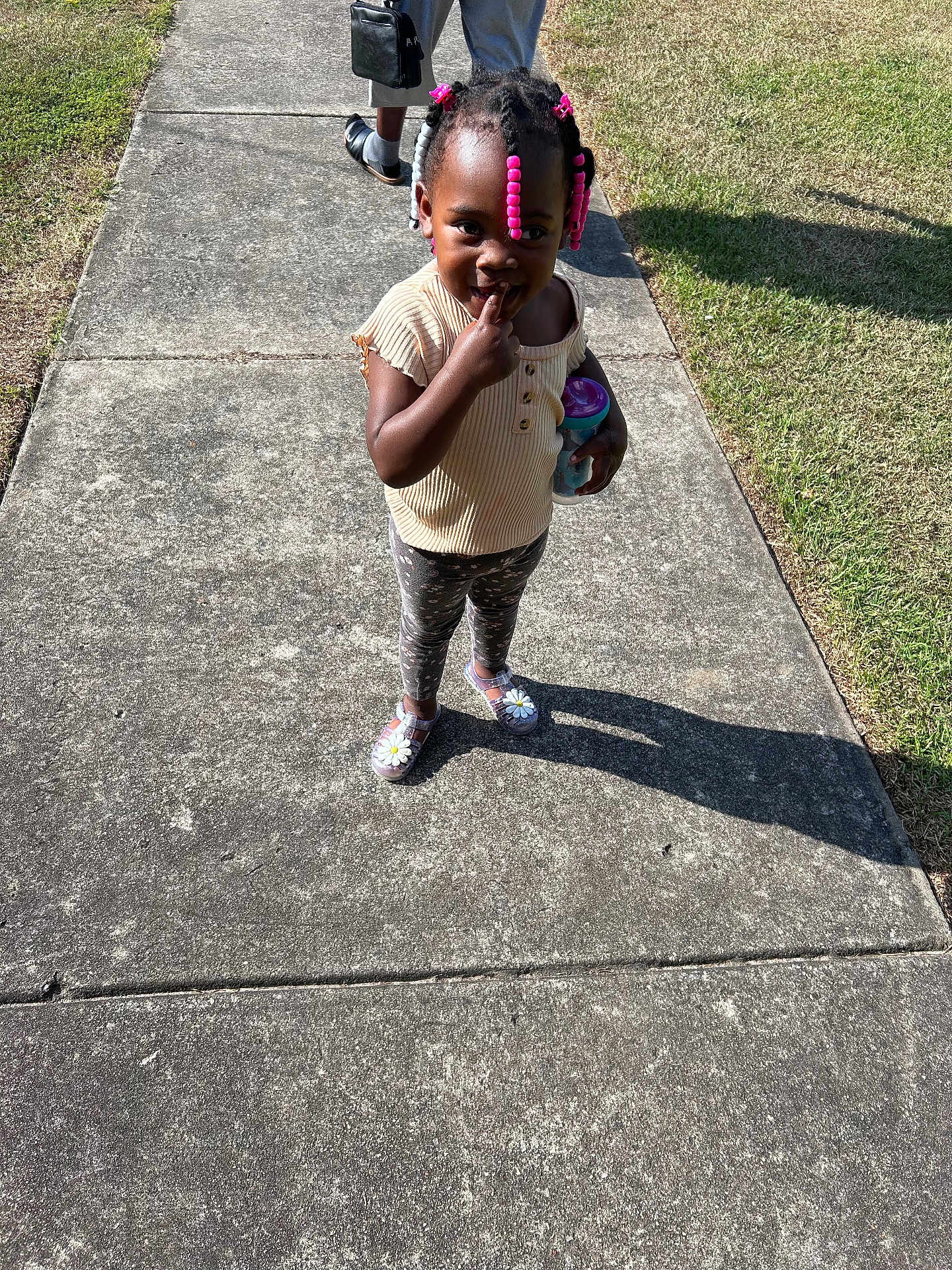 Hazeleigh is registered to the contest to win money with this photo: toddler, child, sidewalk, outdoor, sunlight, shadow, grass, beads, hair, pink, clothing, sippy_cup, playful, person, footwear, patterned_pants, short_sleeve_shirt, cute, smiling, standing