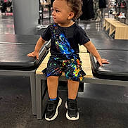 Zidane is registered to the contest to win money with this photo: child, boy, sitting, bench, clothing, tshirt, shorts, shoes, store, shopping, curly_hair, floor, black_shoes, colorful_clothes, indoor, retail, fashion, casual, portrait, young