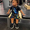 child, boy, sitting, bench, clothing, tshirt, shorts, shoes, store, shopping, curly_hair, floor, black_shoes, colorful_clothes, indoor, retail, fashion, casual, portrait, young