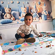Maëlio participe au concours pour gagner de l'argent avec cette photo : toddler, birthday_party, table, confetti, candy, decorations, plush_toys, teddy_bears, party_hats, child, curious, sitting, clothing, suspenders, jeans, indoor, celebration, smile, face, cute