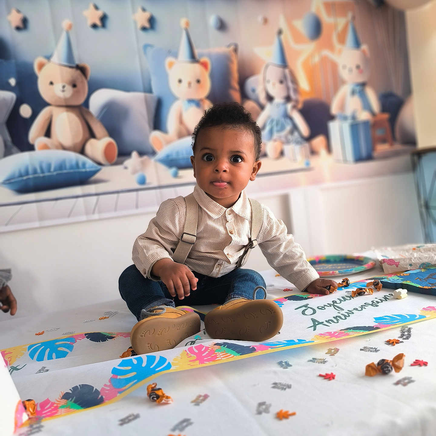 Maëlio participe au concours pour gagner de l'argent avec cette photo : birthday_party, candy, celebration, child, clothing, confetti, curious, cute, decorations, face, indoor, jeans, party_hats, plush_toys, sitting, smile, suspenders, table, teddy_bears, toddler