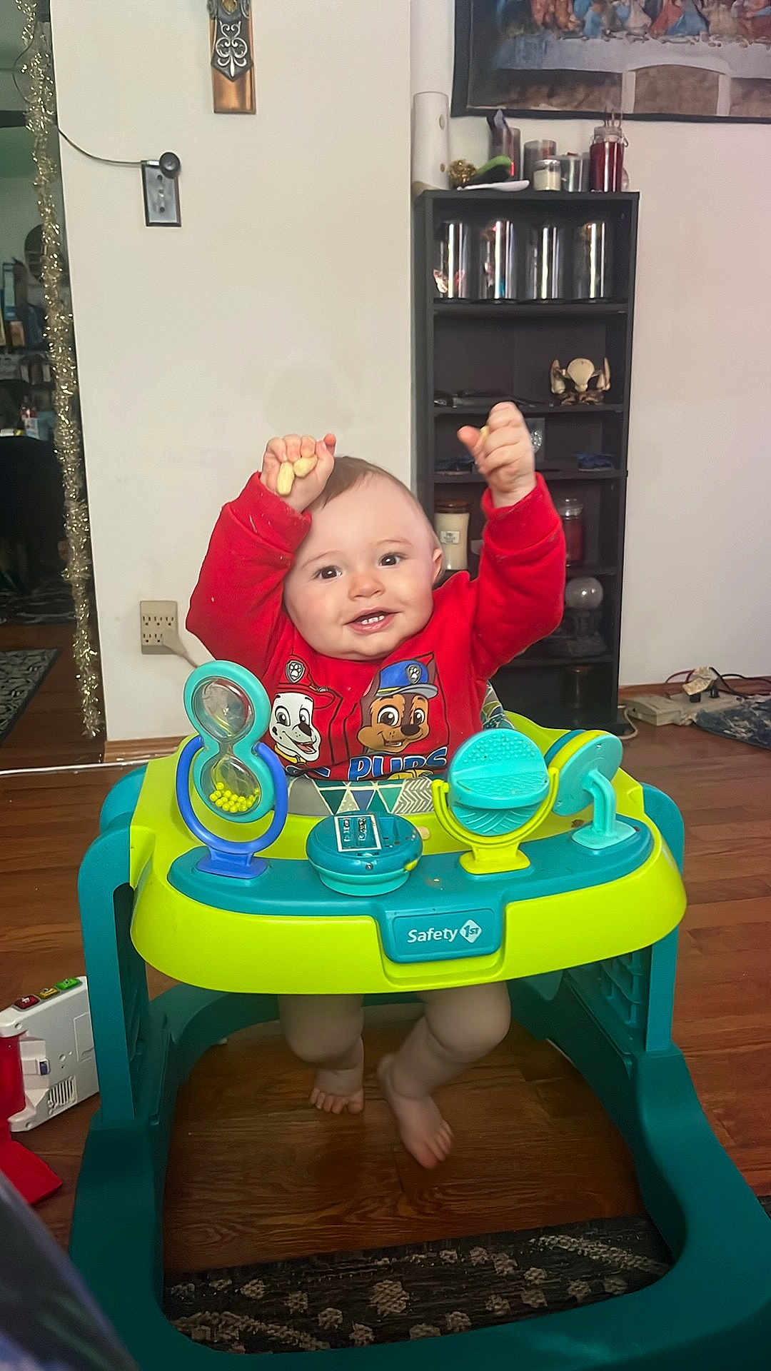 Waylon is registered to the contest to win money with this photo: baby, child, walker, red_clothing, indoor, toy, smiling, happy, raising_hands, furniture, wooden_floor, shelf, decor, person, face, footwearless, floor_rug, household, cute, home