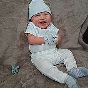 Emmanuel is registered to the contest to win money with this photo: baby, infant, child, smiling, happy, portrait, sitting, couch, blanket, hat, mittens, stuffed_animal, bear, clothing, white_outfit, socks, pacifier, indoor, cozy, close_up
