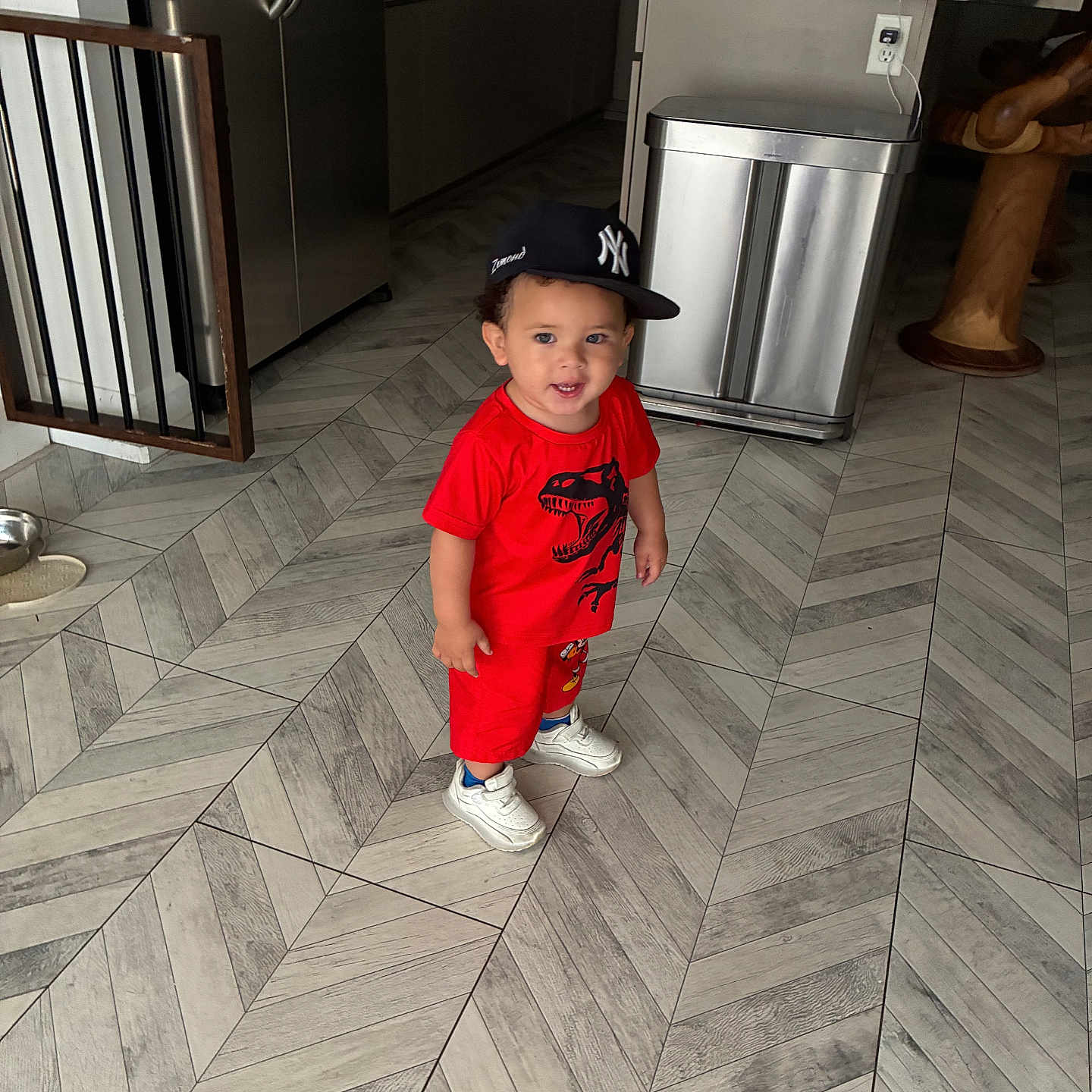 Zamond is registered to the contest to win money with this photo: toddler, child, red_clothing, baseball_cap, smile, indoor, kitchen, floor_tiles, modern_interior, trash_can, refrigerator, wooden_stool, white_sneakers, person, happy, standing, young_child, casual_wear, headwear, cute