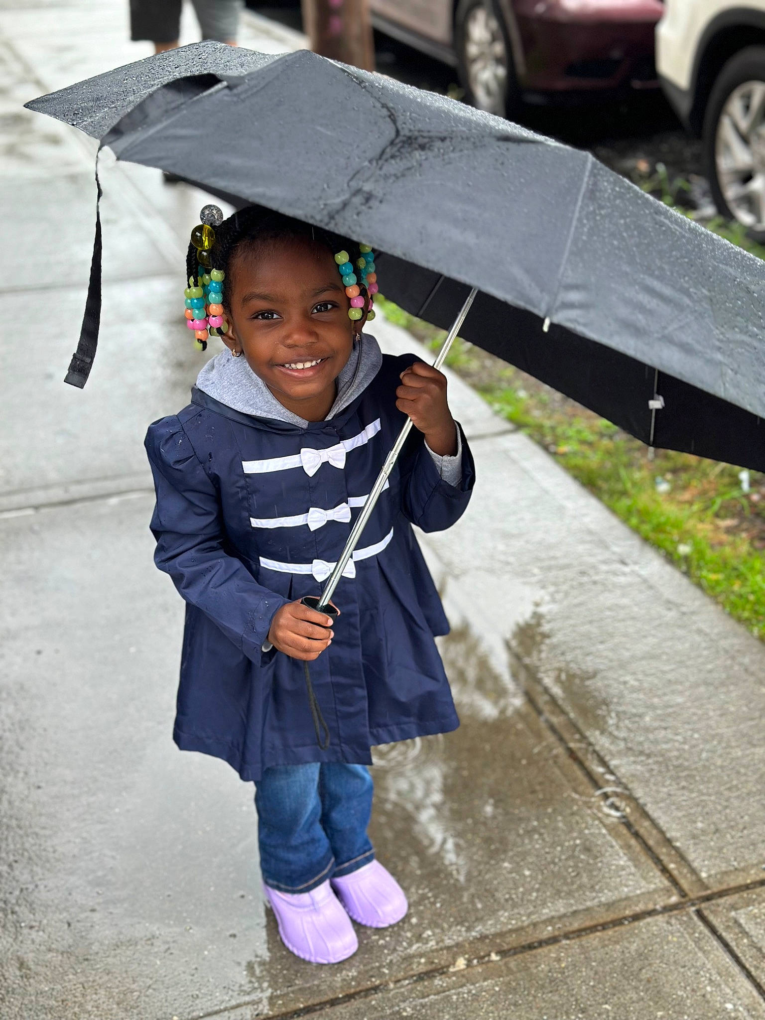 Leighton is registered to the contest to win money with this photo: asphalt, automotive_design, automotive_exterior, automotive_tire, black, bumper, child, fashion_accessory, fender, happy, joy, motor_vehicle, person, public_space, road, road_surface, sidewalk, smile, tire, toddler