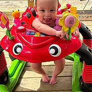 Alora joined the competition — help win amazing prizes! baby, child, colorful, deck, feet, flower, green, happy, infant, outdoor, person, plastic, playful, red, smiling, summer, tongue_out, toy, walker, yellow