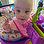 Alora is registered to the contest to win money with this photo: baby, infant, child, pink_bib, activity_center, toy, colorful, indoor, curious, wide_eyes, hand, face, early_childhood, playtime, seat, window, natural_light, close_up, smiling, person