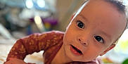Alora is registered to the contest to win money with this photo: baby, blanket, child, closeup, clothing, curious, cute, expression, eyes, face, hand, indoors, infant, long_sleeve, lying_down, mouth, patterned, portrait, quilt, soft_light