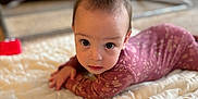 Alora joined the competition — help win amazing prizes! baby, blanket, blurred_background, child, curious, cute, eyes, face, furniture, hands, indoor, infant, living_room, lying_down, onesie, portrait, purple_clothing, quilt, soft_lighting, table