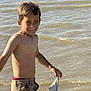 boy, child, shirtless, water, river, cloth, holding, standing, outdoor, summer, playful, smiling, shorts, nature, young, person, sunlight, fun, casual, wet