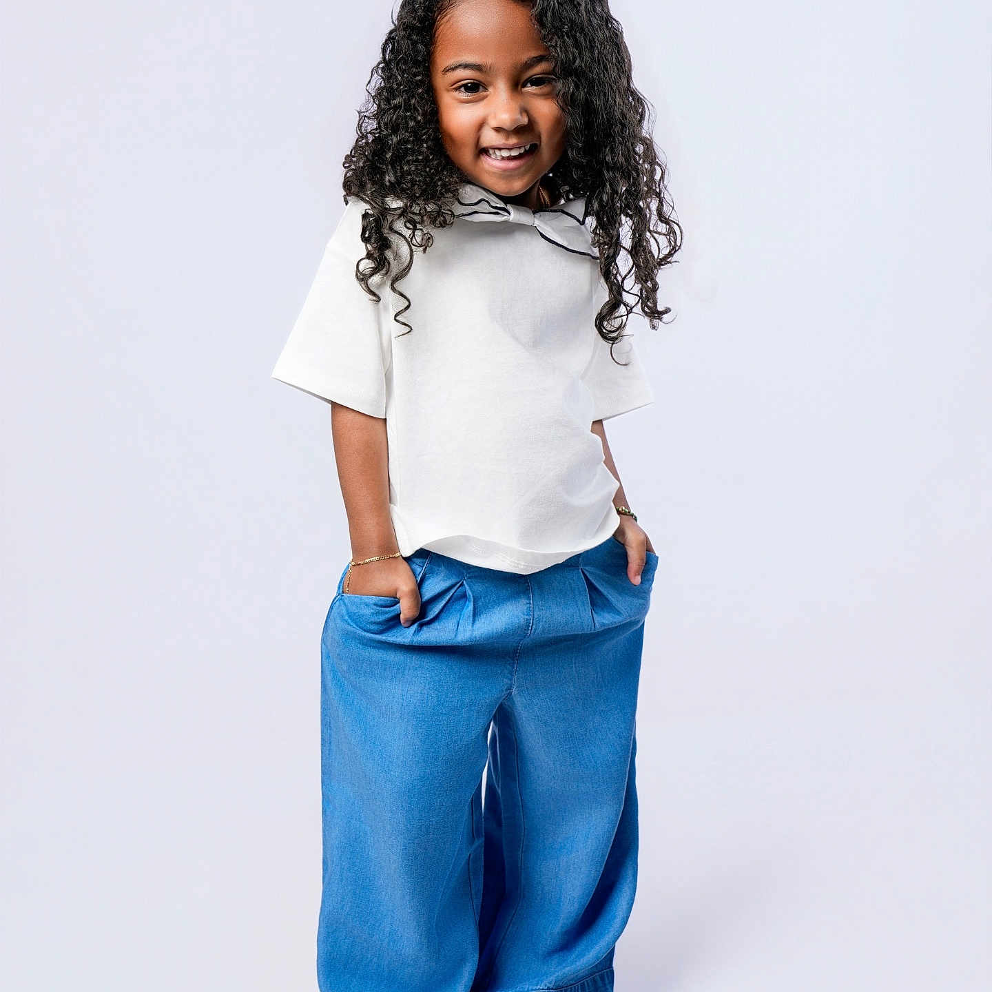 Kasey Gutierrez joined the competition — help win amazing prizes! child, smiling, curly_hair, barefoot, blue_pants, white_top, standing, hands_in_pockets, happy, portrait, studio, fashion, casual, clothing, person, cute, young, full_length, isolated, background