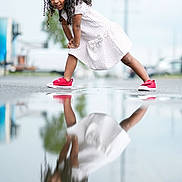 Kasey Gutierrez is registered to the contest to win money with this photo: child, girl, reflection, puddle, red_shoes, white_dress, curly_hair, outdoor, urban, street, playful, smiling, pose, casual, daytime, young, person, fashion, fun, photography