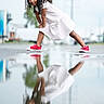 child, girl, reflection, puddle, red_shoes, white_dress, curly_hair, outdoor, urban, street, playful, smiling, pose, casual, daytime, young, person, fashion, fun, photography