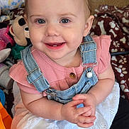 Mylah joined the competition — help win amazing prizes! baby, child, toddler, smiling, face, eyes, denim_overalls, pink_shirt, white_skirt, hands, toys, plush_toy, blanket, carpet, sitting, portrait, indoors, ponytail, teeth, playtime